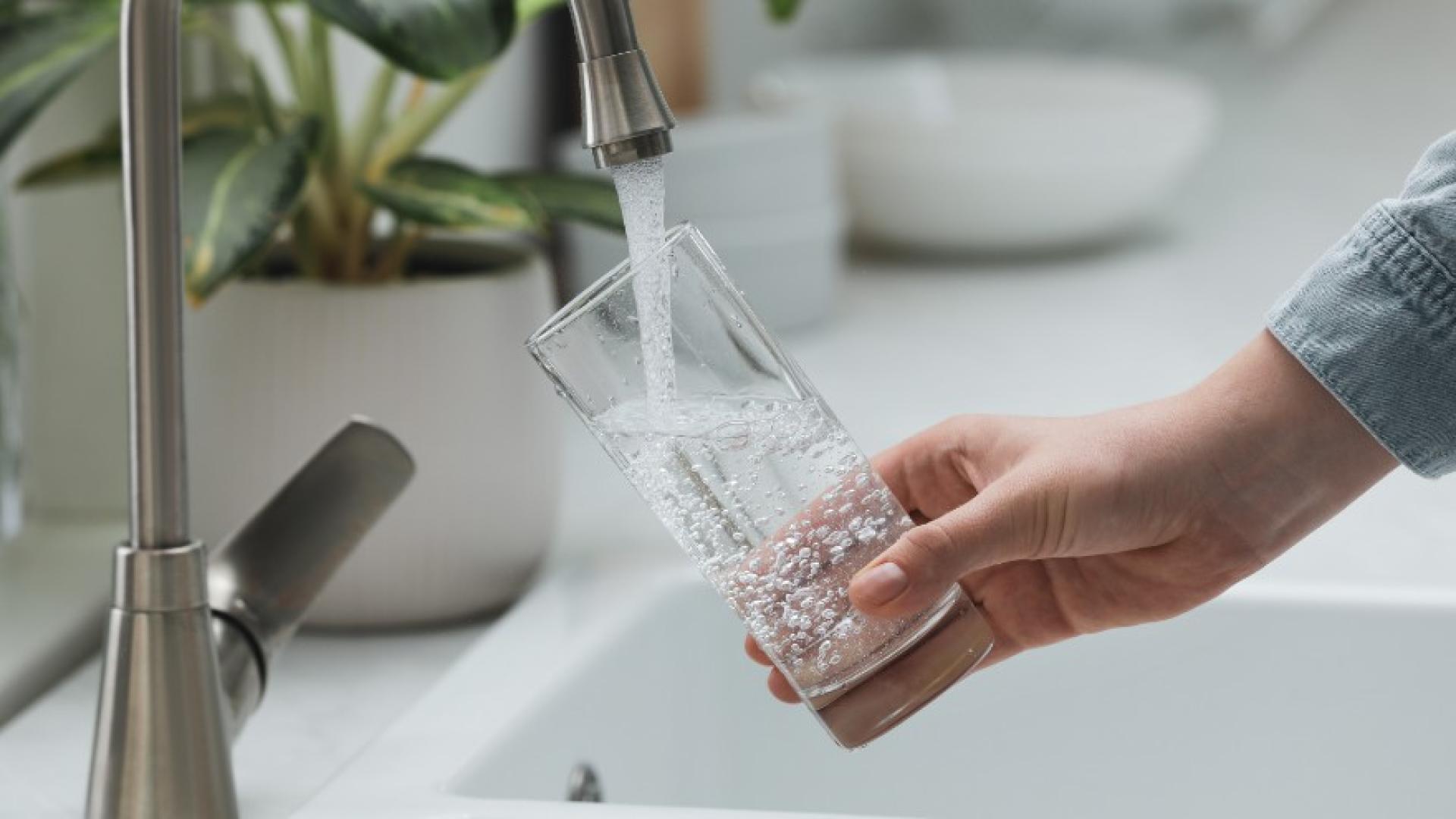 Person filling glass with water under a kitchen sink