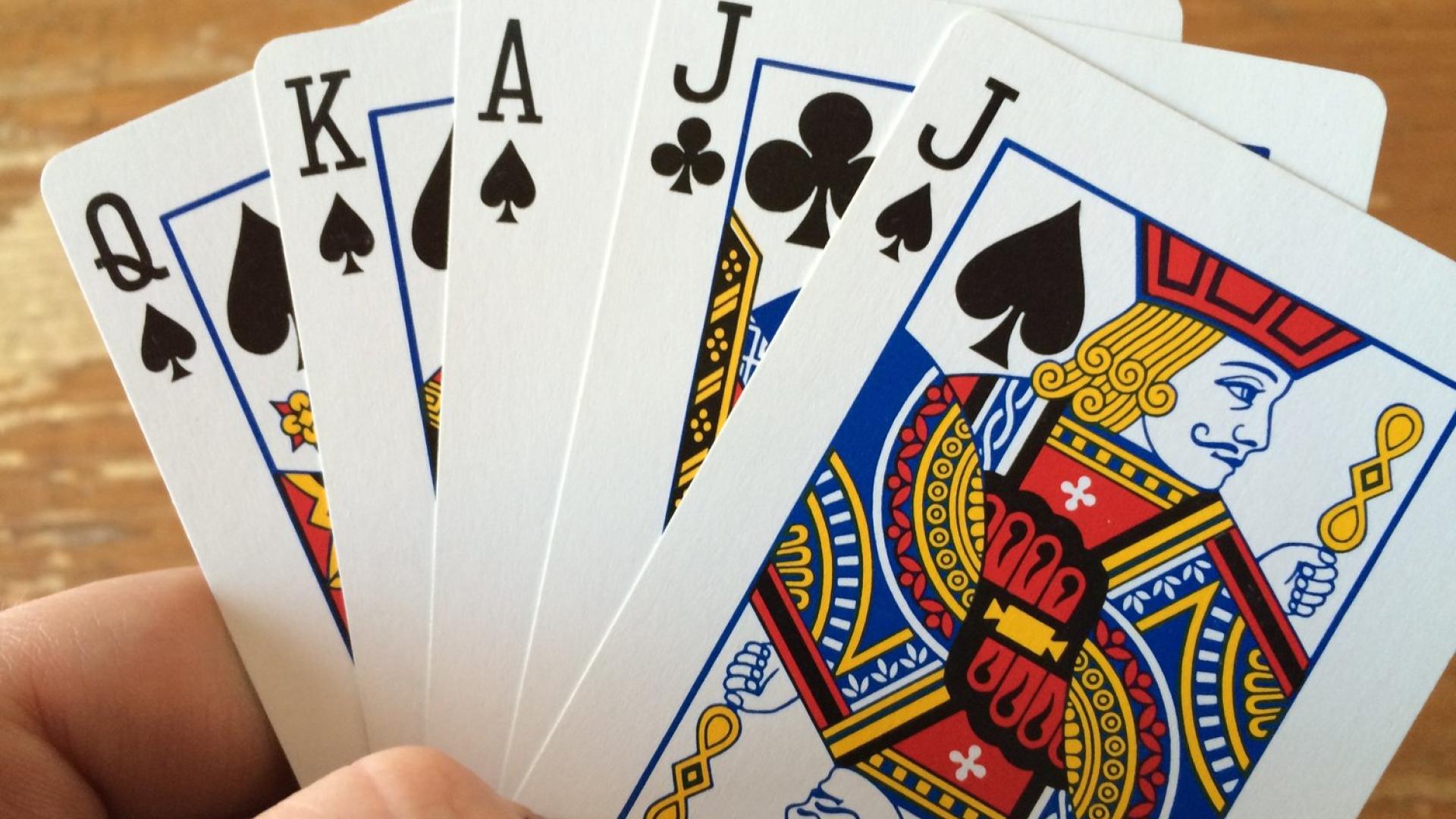 A hand holding a royal flush in spades with a jack of clubs.