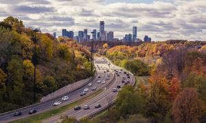 A highway with cars on it and trees with a city in the background